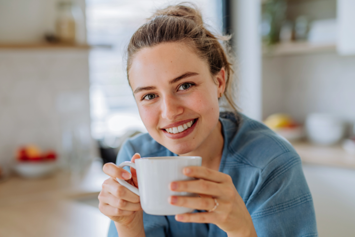 Junge Frau mit Dutt sitzt am Tisch und hält eine Tasse.